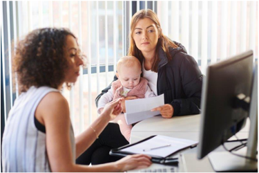 woman sitting at computer helping a woman and her baby