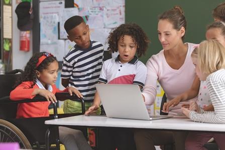 Front view of a teacher and school kids discussing over laptop in classroom at schoo